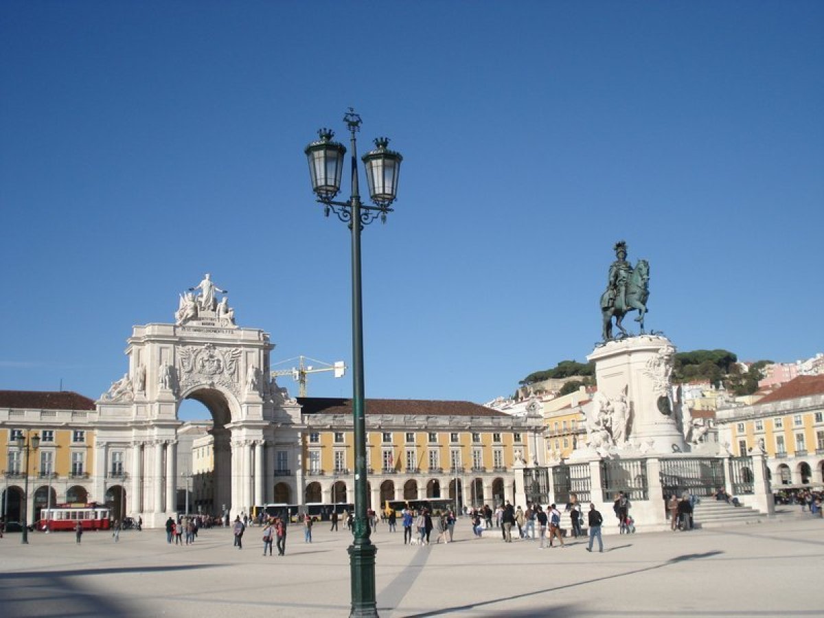 A large building with arches in a bustling commercial square in Lisbon showcases its architectural beauty.