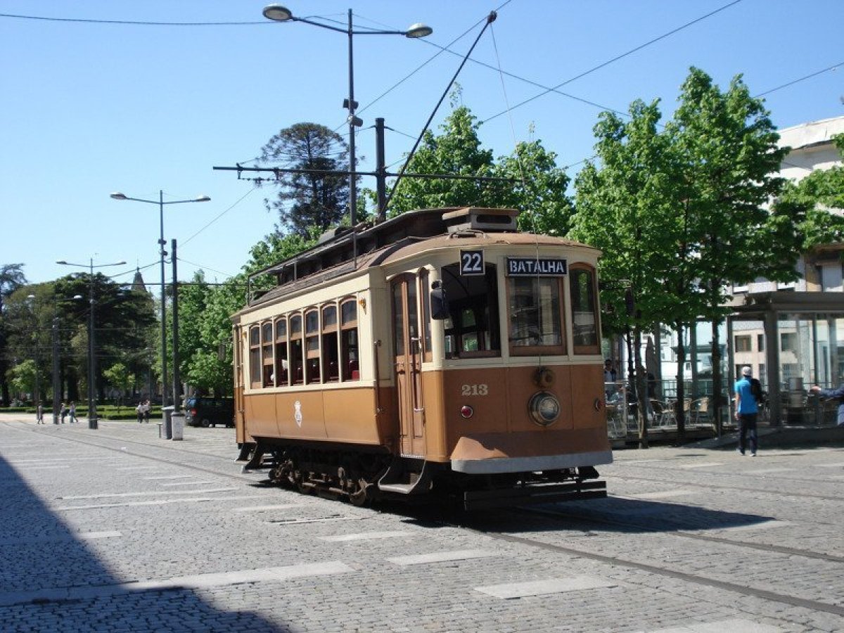 A vintage brown and tan trolley glides through the charming streets of Porto, showcasing the city's rich history.