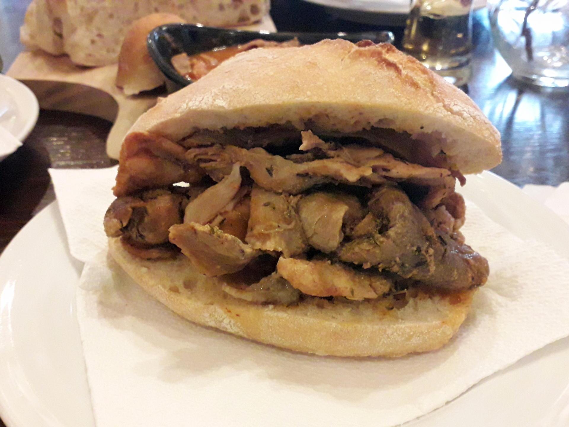 A delicious bifana pork sandwich on a white plate, showcasing the flavors of Braga during a food tour.