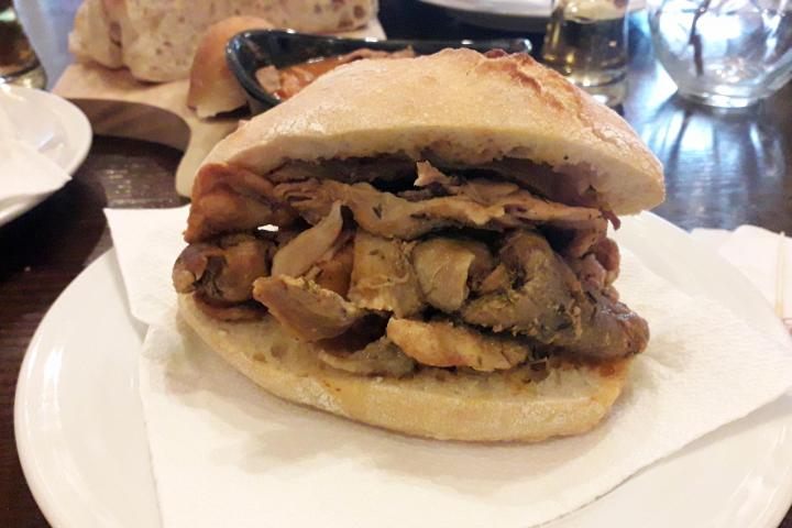 A delicious bifana pork sandwich on a white plate, showcasing the flavors of Braga during a food tour.