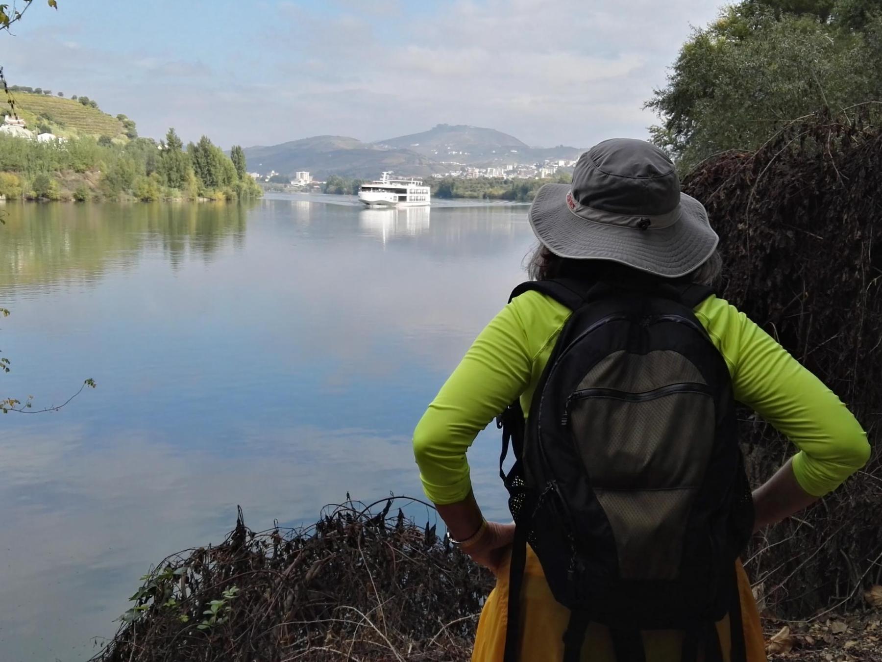A solo traveler admires the Douro River, backpack on her back, enjoying the beauty of nature.
