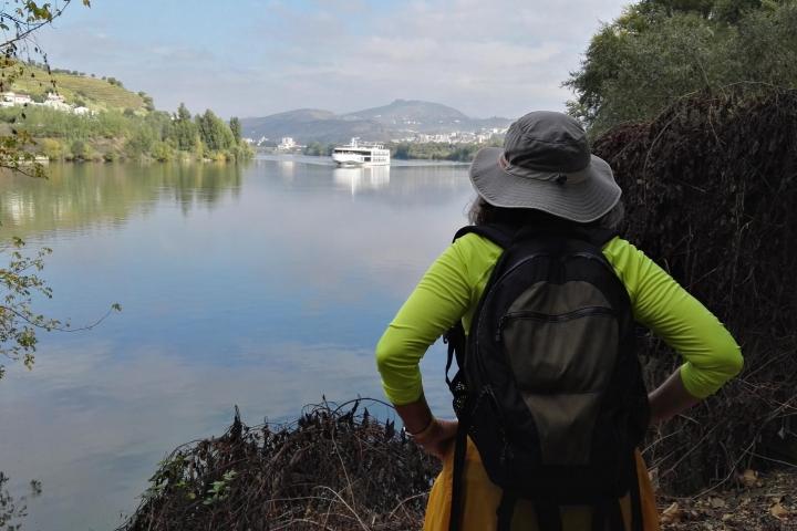 A solo traveler admires the Douro River, backpack on her back, enjoying the beauty of nature.