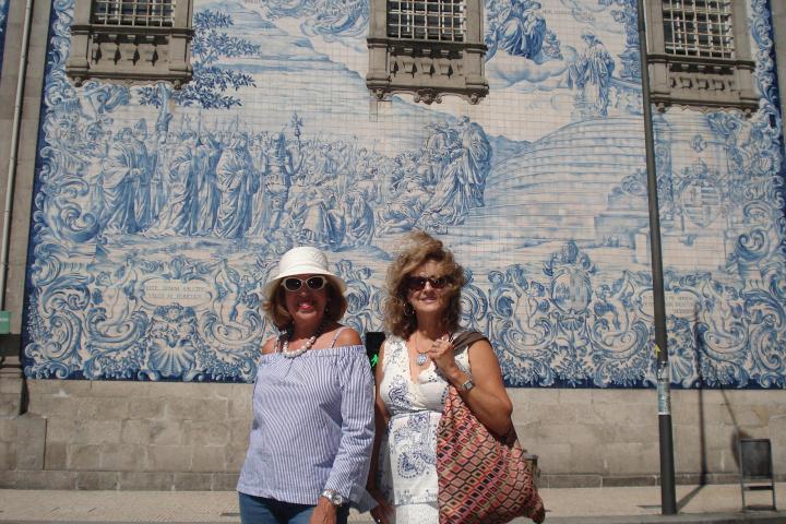 Two women pose in front of a beautiful building during their walking tour in Porto, smiling and enjoying the scenery.