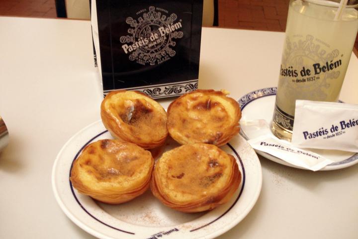 A tempting plate of custard tarts sits on a table in Lisbon, highlighting their rich, creamy texture and flaky pastry.