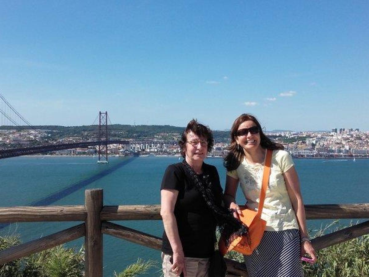 On the April 25 Bridge in Lisbon, two women enjoy the view of the tranquil water below, capturing a moment of connection.