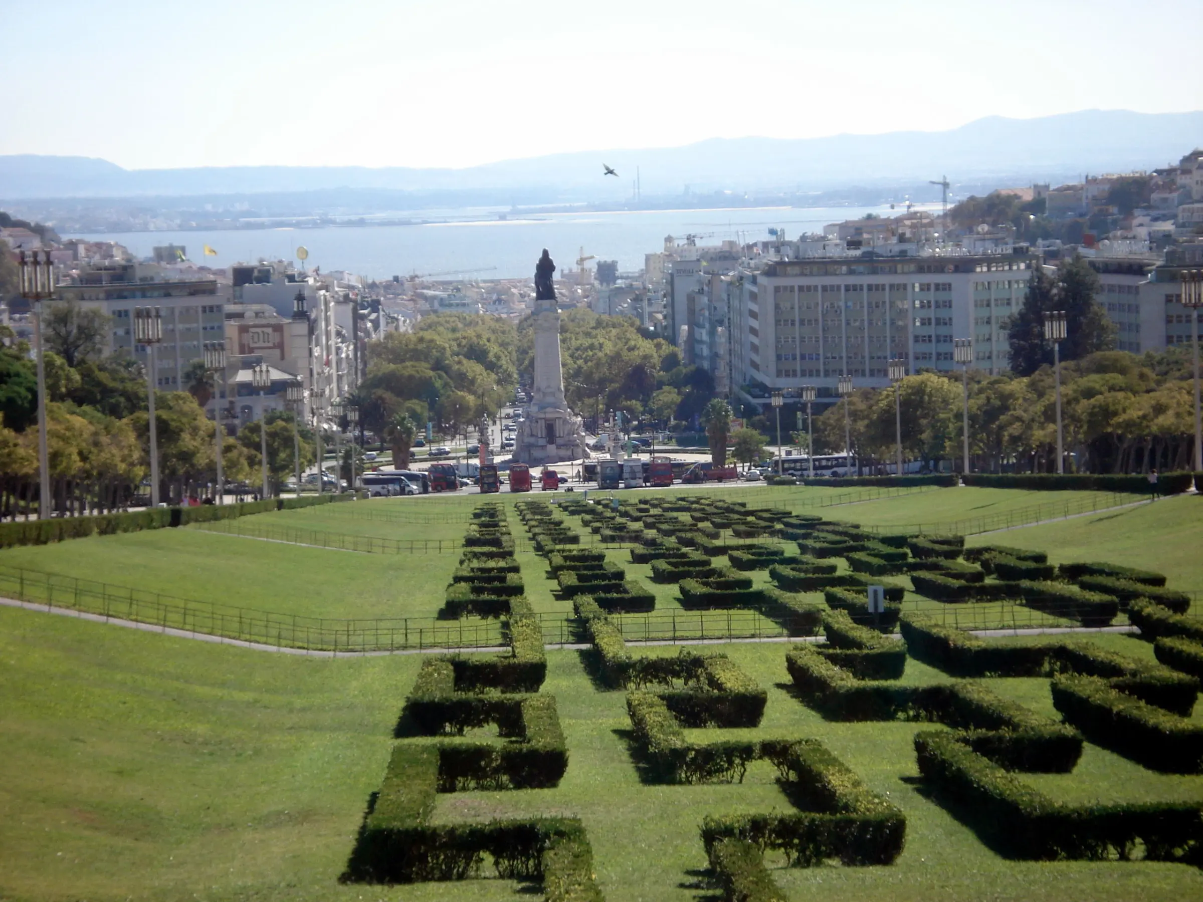 A scenic view from Park Eduardo VII in Lisbon, showcasing lush green gardens with the cityscape and distant hills in the background.