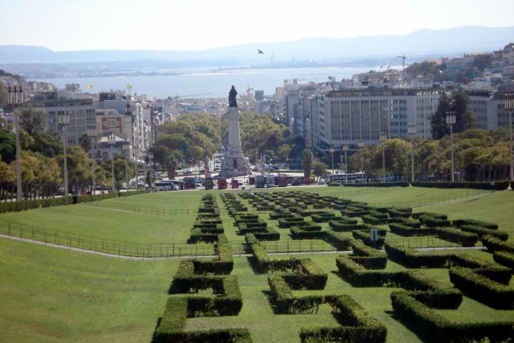 A scenic view from Park Eduardo VII in Lisbon, showcasing lush green gardens with the cityscape and distant hills in the background.