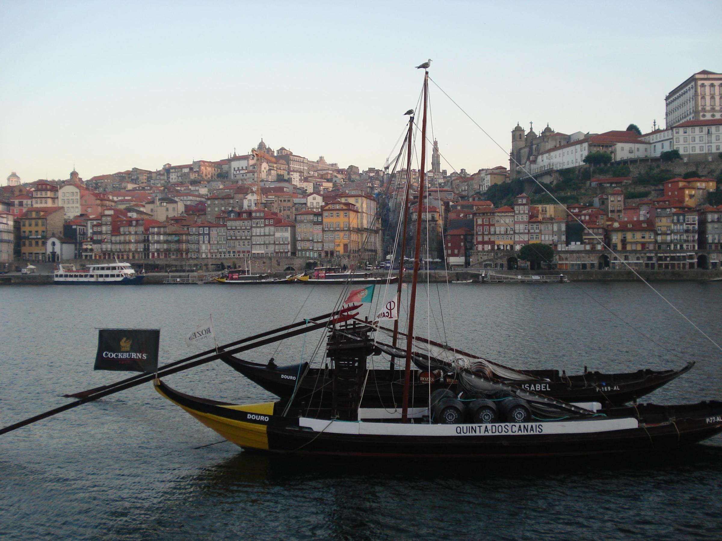 A traditional rabelo boat featuring a large wooden mast navigates the scenic waters of Porto on a city walking tour.