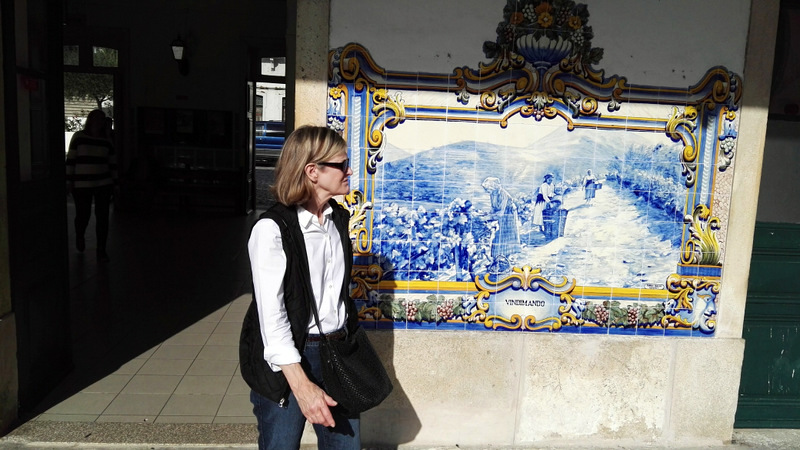 A woman poses gracefully in front of a stunning blue and white tile wall, capturing the essence of Douro Valley tours.
