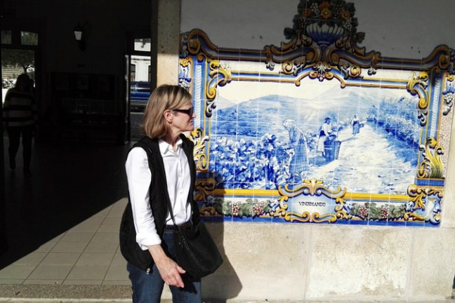 A woman poses gracefully in front of a stunning blue and white tile wall, capturing the essence of Douro Valley tours.