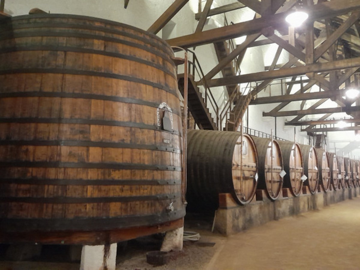 A large wooden barrel sits in a cozy room, complemented by a staircase, evoking the charm of Douro Valley tours.