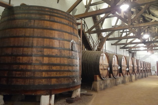A large wooden barrel sits in a cozy room, complemented by a staircase, evoking the charm of Douro Valley tours.