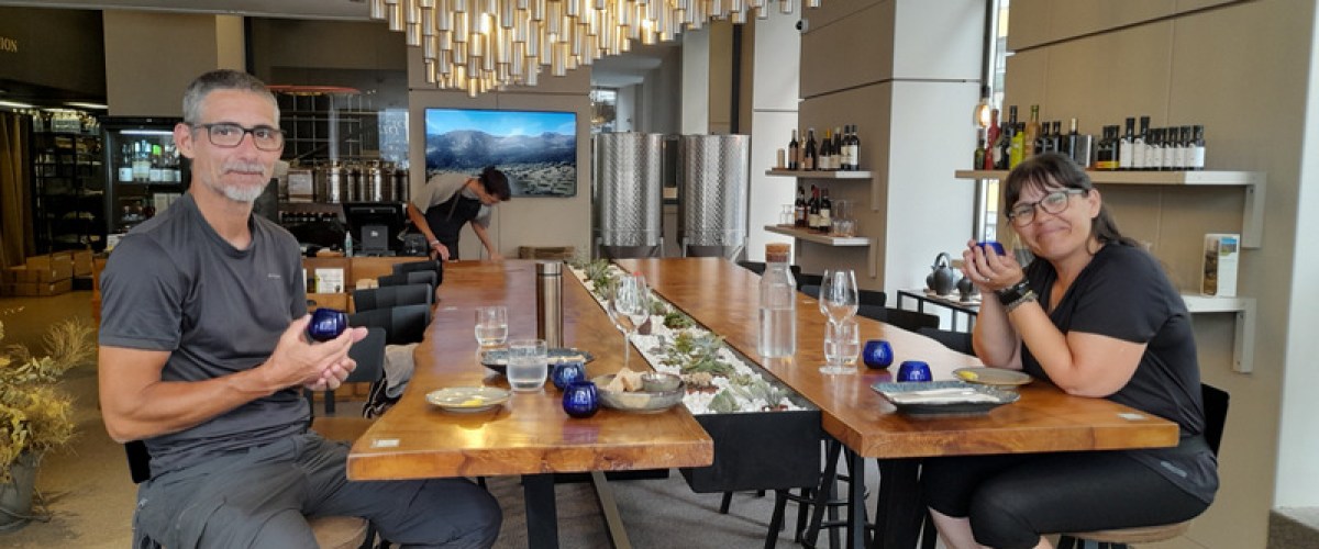 A couple savoring olive oil at a table, each holding a drink, immersed in a delightful tasting experience.
