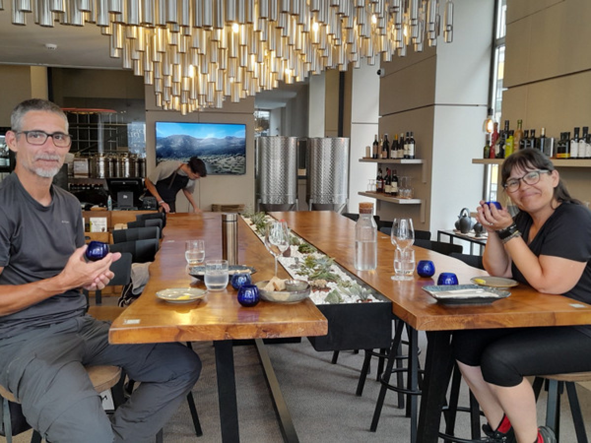 A couple savoring olive oil at a table, each holding a drink, immersed in a delightful tasting experience.