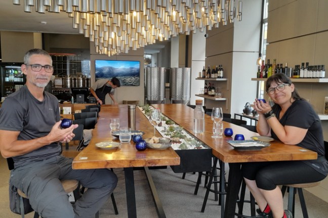 A couple savoring olive oil at a table, each holding a drink, immersed in a delightful tasting experience.