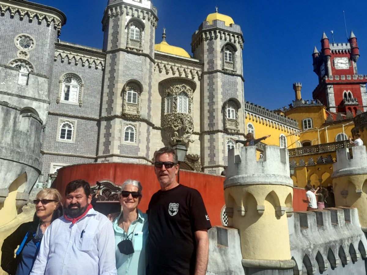 A small group of tourists poses in front of the stunning Pena Palace in Sintra, surrounded by vibrant colors and architecture.