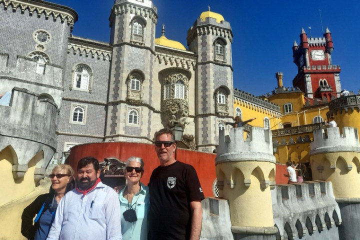 A small group of tourists poses in front of the stunning Pena Palace in Sintra, surrounded by vibrant colors and architecture.