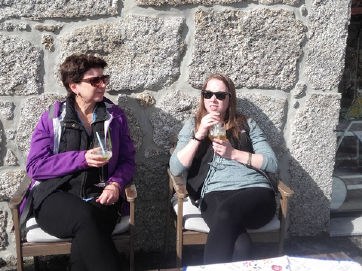 Two women sitting on a chair, one savoring a refreshing Portuguese sangria, enjoying a sunny day together.
