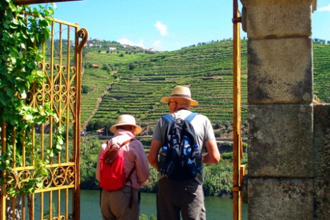 A pair of seniors looks out through a gate, taking in the stunning vistas of the Douro Valley on their hike.