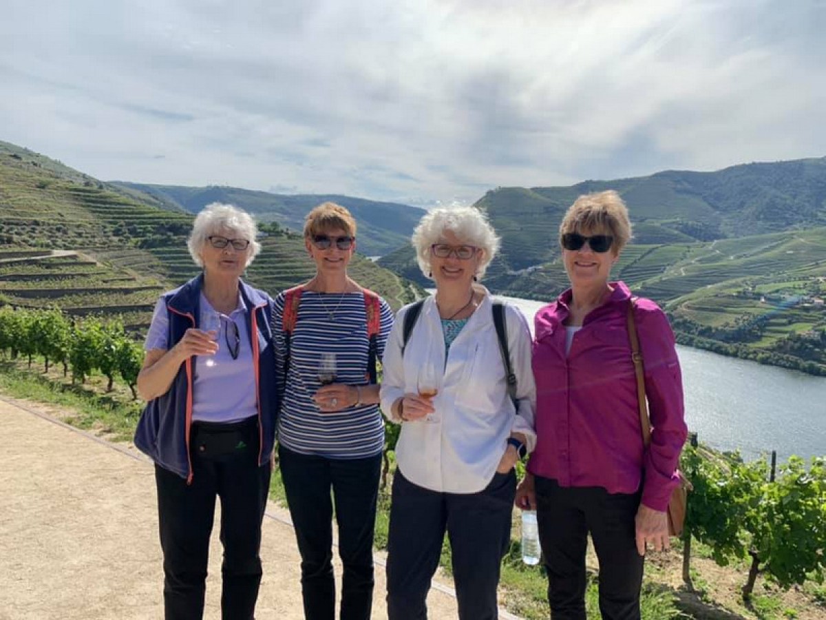 Four senior women in the Douro Valley raise their wine glasses, smiling joyfully for a memorable photo together.