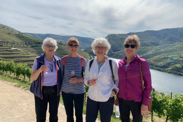 Four senior women in the Douro Valley raise their wine glasses, smiling joyfully for a memorable photo together.