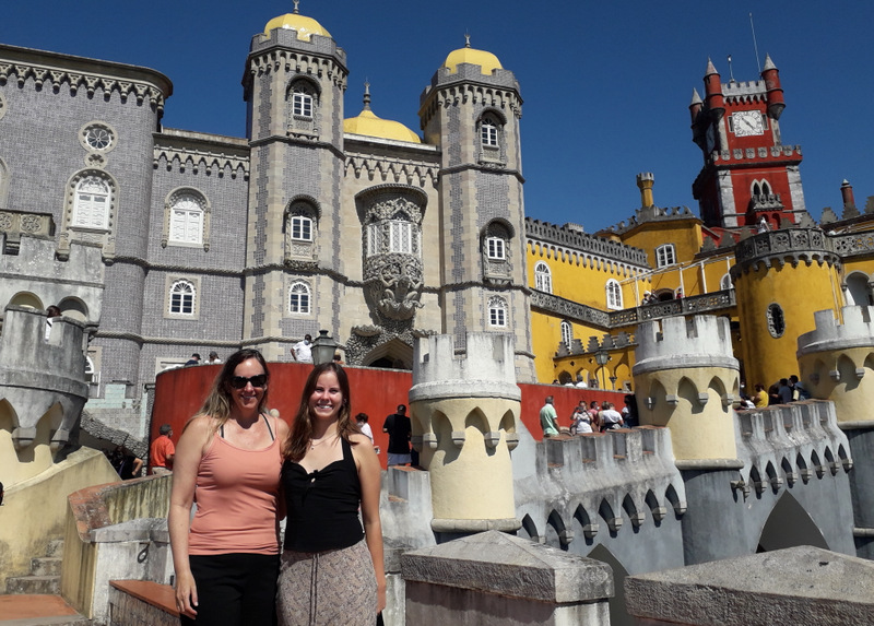 A mother and daughter pose together in front of the stunning Pena Palace in Sintra, showcasing their joyful bond.