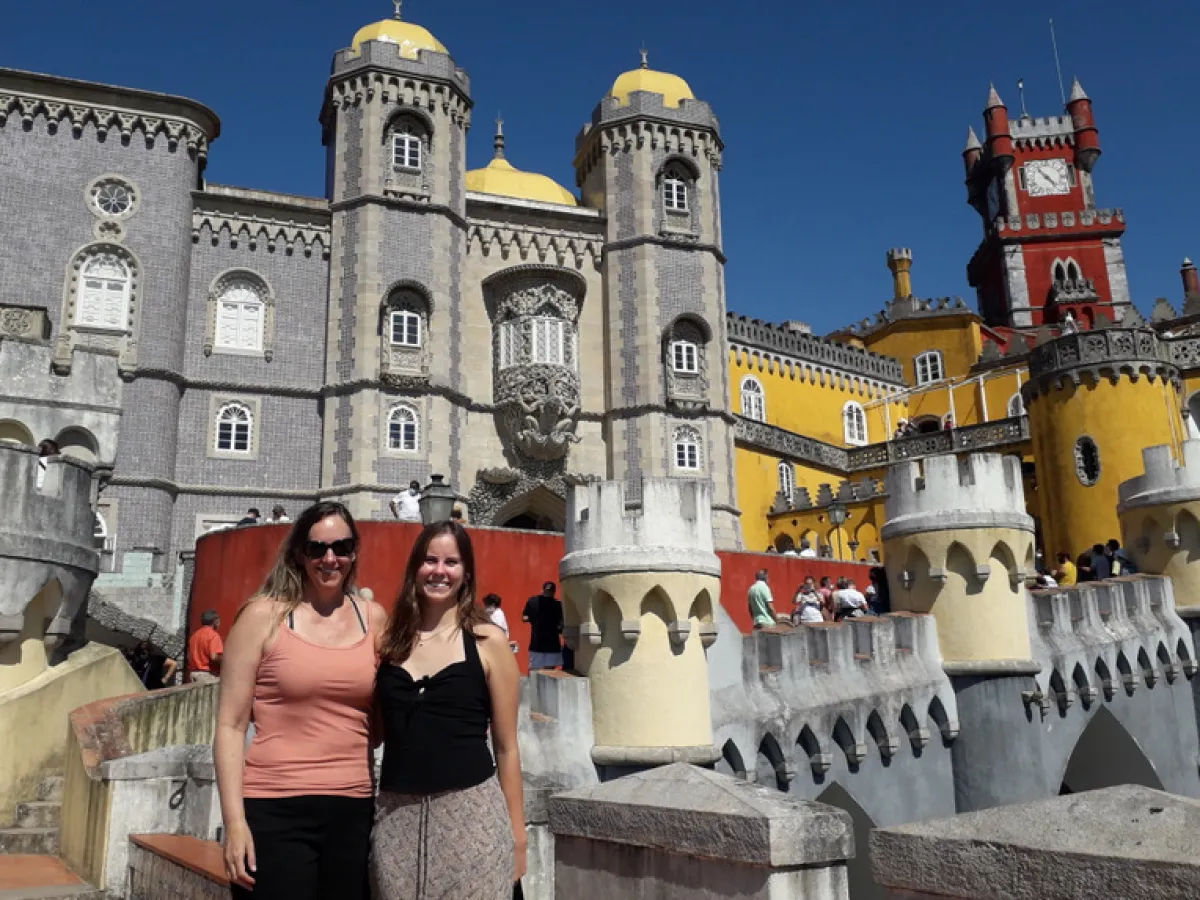 A mother and daughter pose together in front of the stunning Pena Palace in Sintra, showcasing their joyful bond.