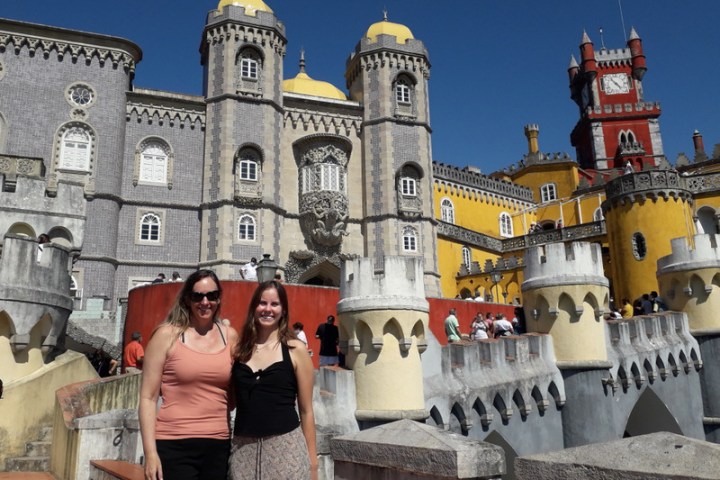 A mother and daughter pose together in front of the stunning Pena Palace in Sintra, showcasing their joyful bond.