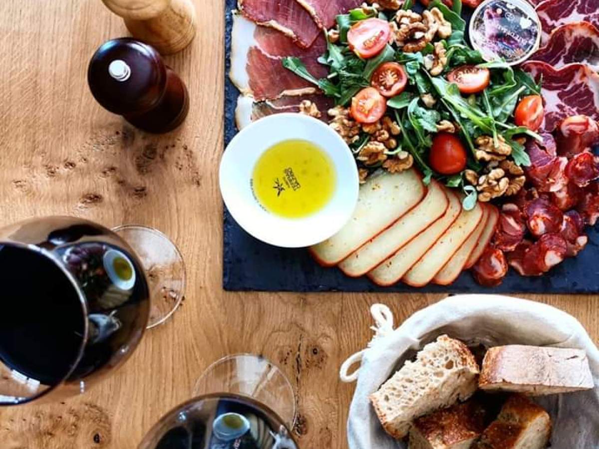 A delicious spread of smoked Portuguese sausages and colorful vegetables, paired with wine glasses, ideal for a culinary adventure.