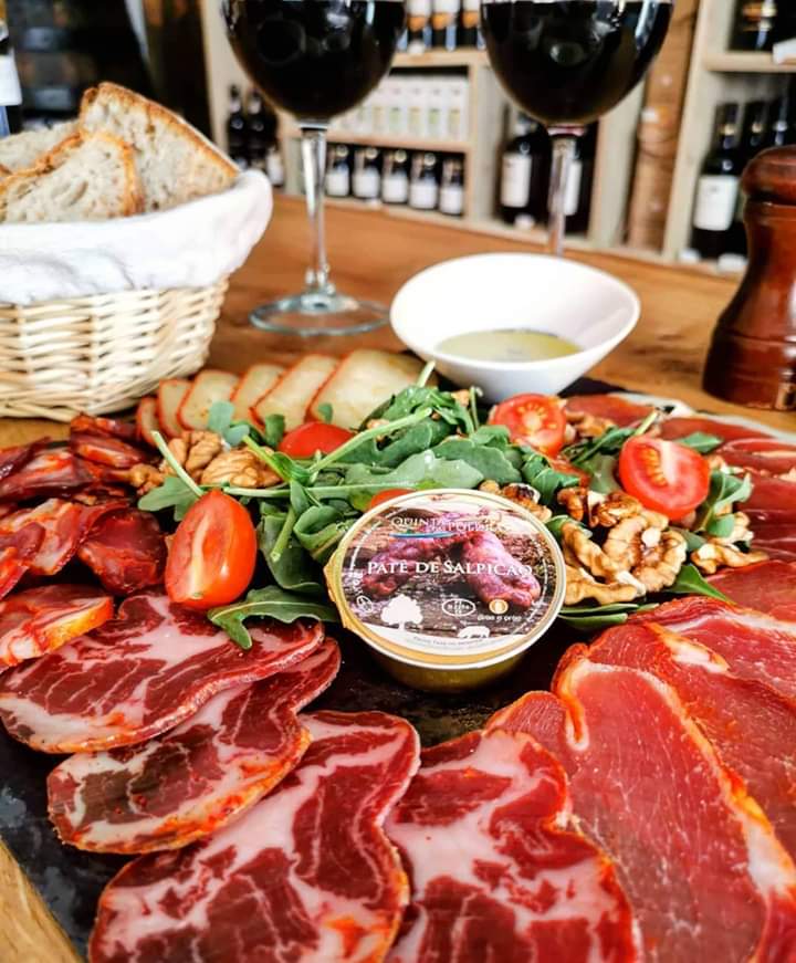 A vibrant platter of smoked Portuguese sausages and fresh vegetables, accompanied by elegant wine glasses, perfect for a food tour.