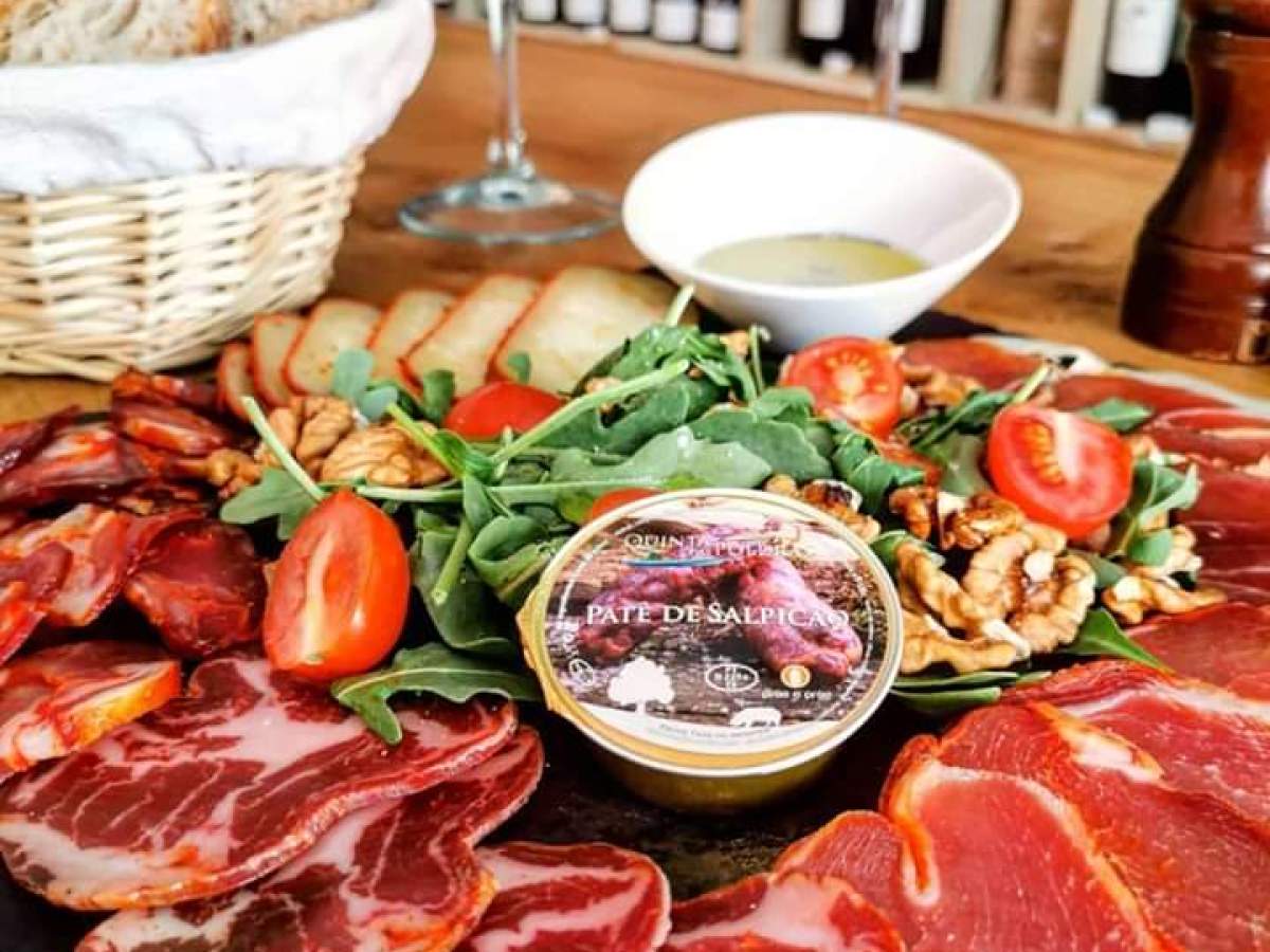 A vibrant platter of smoked Portuguese sausages and fresh vegetables, accompanied by elegant wine glasses, perfect for a food tour.