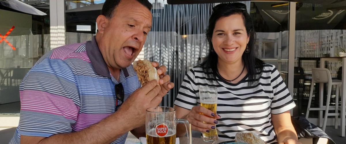 A couple savoring a bifana sandwich and enjoying beers during a delightful food tour in Braga.