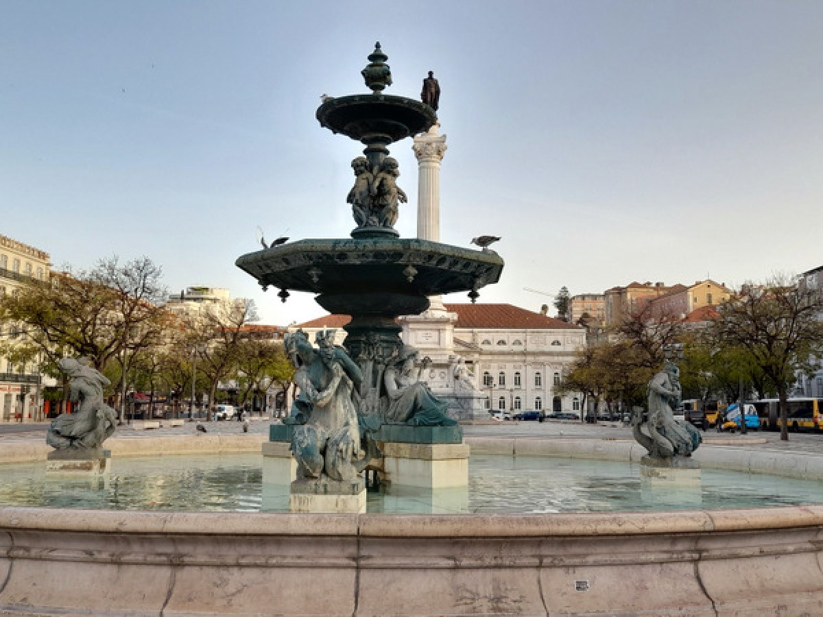 a fountain in front of a statue rossio lisbon