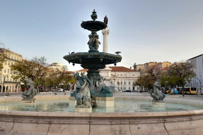 a fountain in front of a statue rossio lisbon