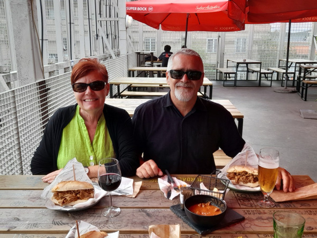 A couple enjoys a meal at a table, sharing delicious bifana sandwiches and gizzards together.