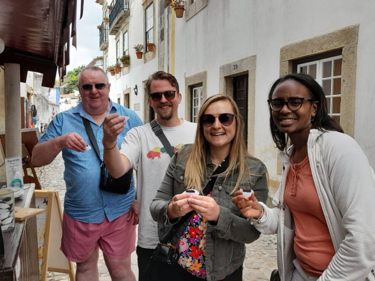 A small group enjoying ginjinha poses cheerfully in front of a charming building in Obidos, capturing a joyful moment.