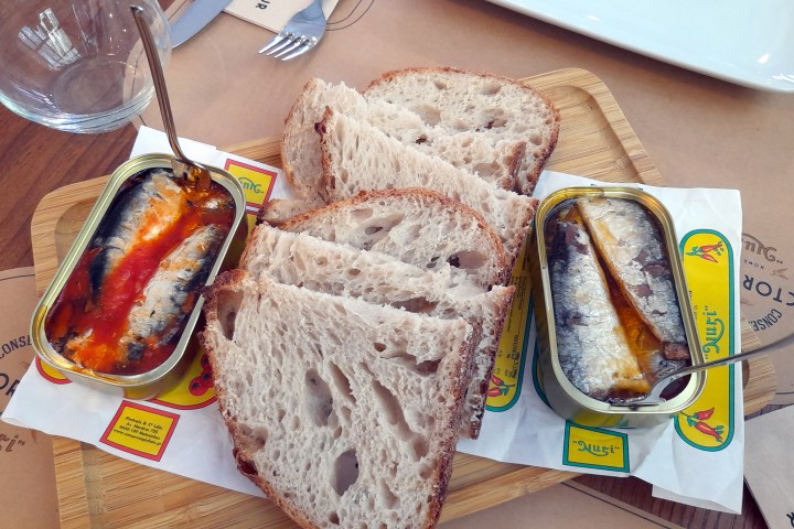 Two cans sit on a wooden cutting board, highlighting a delicious Portuguese food tour with sardines and bread.