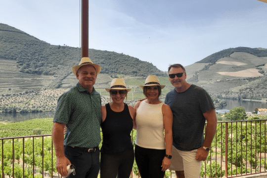 Four friends stand on a balcony, admiring the majestic mountains of Douro Valley after a memorable hiking tour.