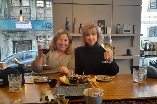 Two women savoring wine together at a table, sharing stories and smiles during a delightful food tour in Portugal.