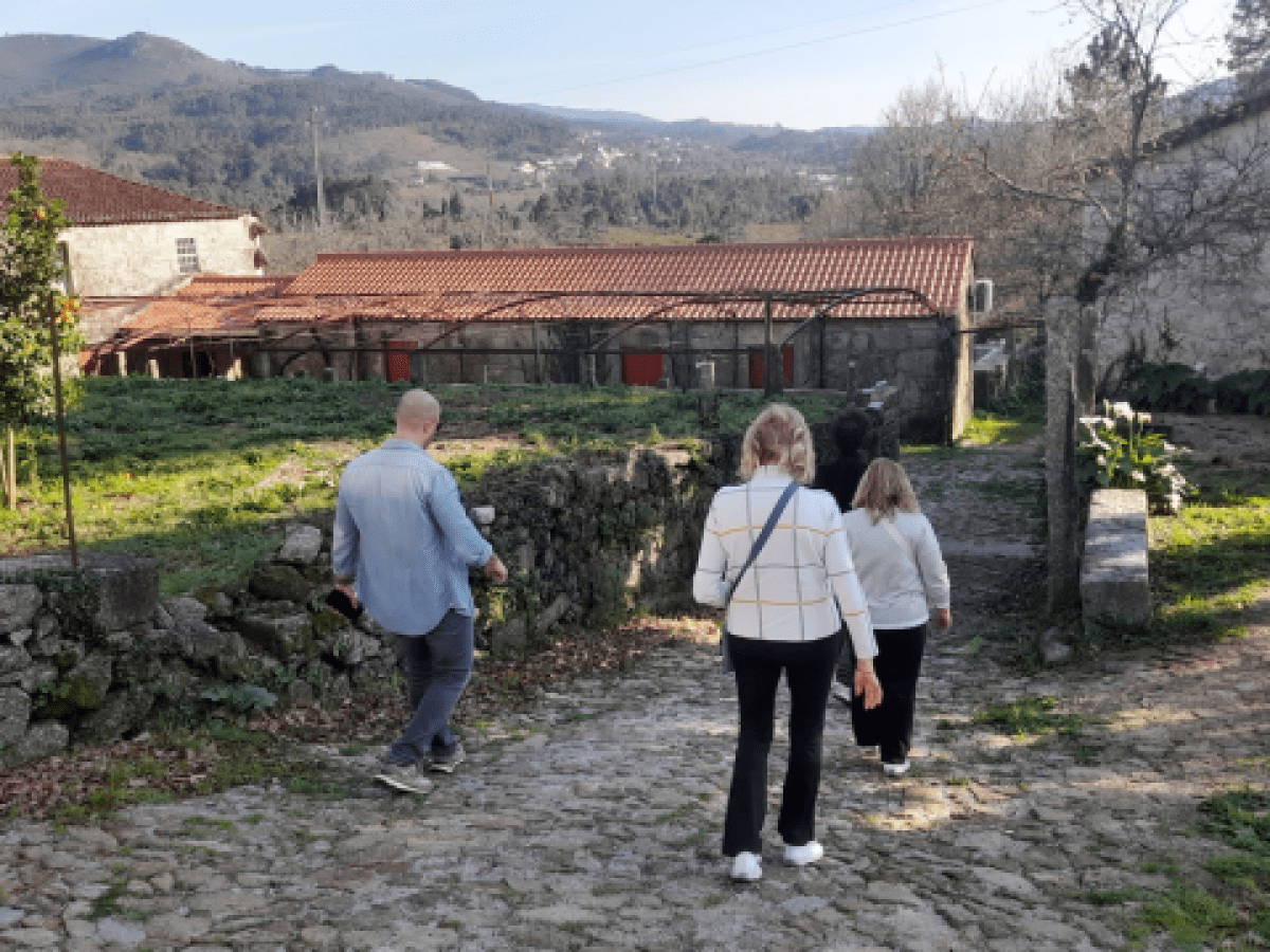 A trio walks along a picturesque path near a house, savoring the experience of a wine farm tour in beautiful Portugal.