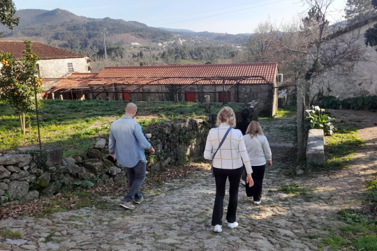 A trio walks along a picturesque path near a house, savoring the experience of a wine farm tour in beautiful Portugal.