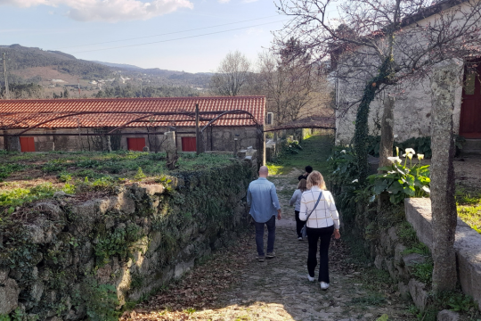 Three visitors walk down a scenic path by a house, savoring the experience of a wine farm tour in beautiful Portugal.