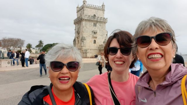Three smiling women pose for a photo in front of Belem Tower during a small group tour in Portugal.