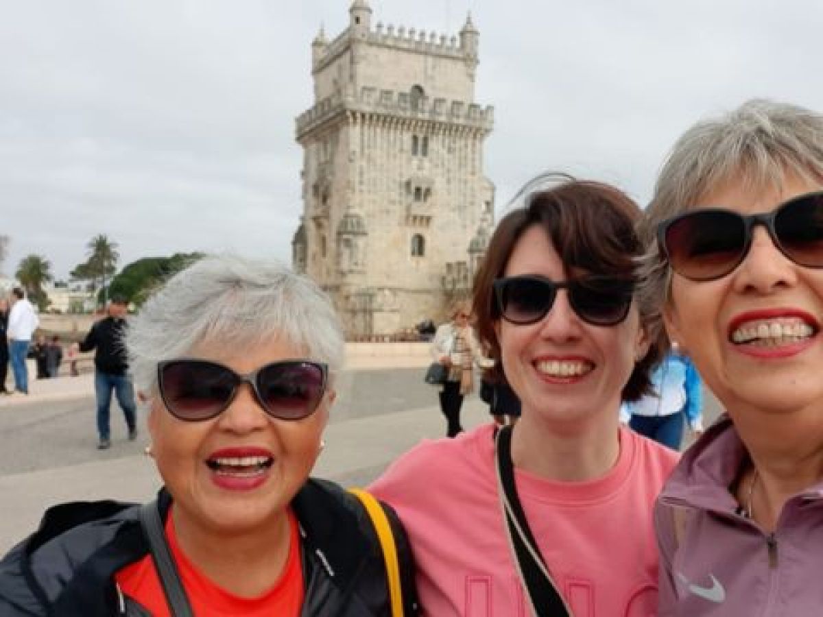 Three smiling women pose for a photo in front of Belem Tower during a small group tour in Portugal.