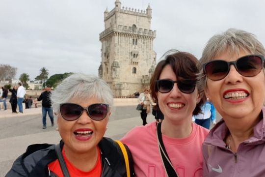 Three smiling women pose for a photo in front of Belem Tower during a small group tour in Portugal.
