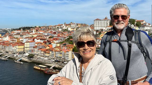 A happy older couple poses in front of a cityscape in Porto, capturing a moment during their enjoyable small group wine and food tour.