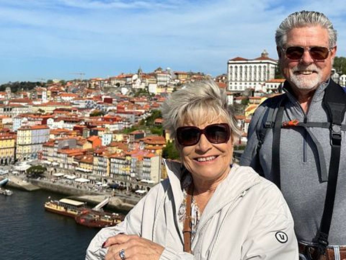 A happy older couple poses in front of a cityscape in Porto, capturing a moment during their enjoyable small group wine and food tour.