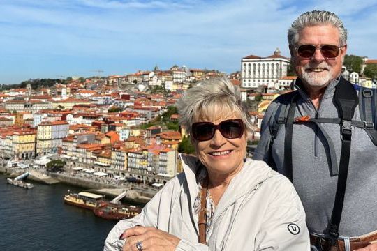 A happy older couple poses in front of a cityscape in Porto, capturing a moment during their enjoyable small group wine and food tour.