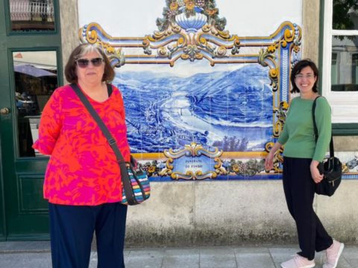 Cris Fonte and a guest stand together in front of a beautiful building, capturing a moment from their 7-day adventure in Portugal.