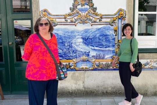 Cris Fonte and a guest stand together in front of a beautiful building, capturing a moment from their 7-day adventure in Portugal.